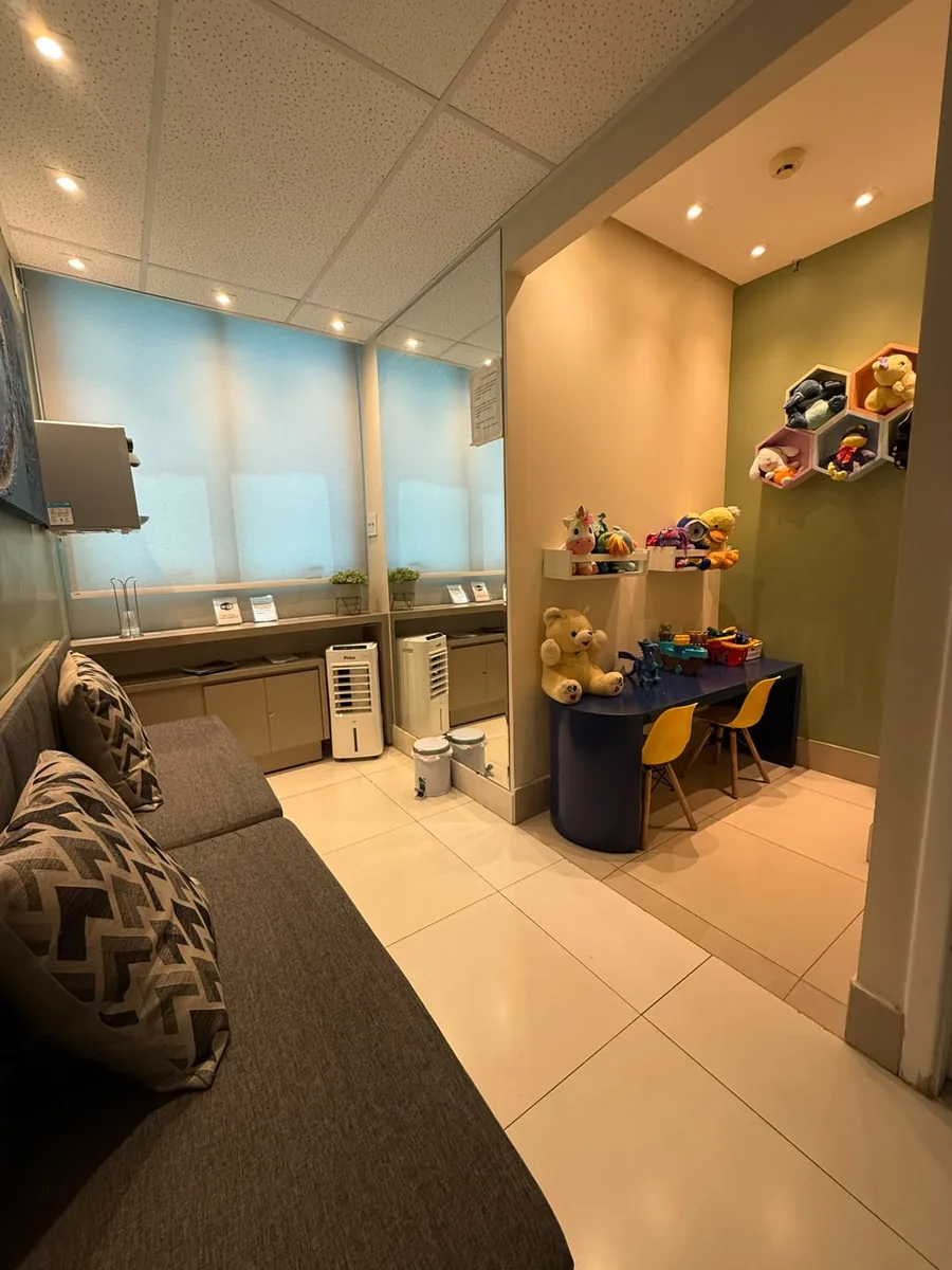 Sala de espera com sofá cinza e cantinho infantil com mesa azul e bichos de pelúcia
